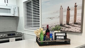 A kitchen with white cabinets, a microwave, and a window with blinds. There is a counter with a bottle of wine, a plant, and a welcome sign. - 2-bedroom with private pool in Fort Myers Beach 2 minute walk to beach (Fort Myers Beach)