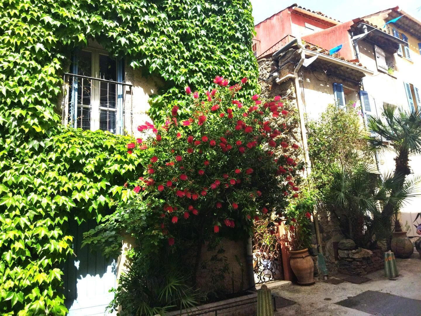 Ein Gebäude mit einer steinernen Fassade, einem roten Dach und einem Garten mit roten Blumen und Grünpflanzen.