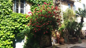Un bâtiment à la façade en pierre, doté d’un toit rouge et d’un jardin agrémenté de fleurs rouges et de feuillage vert.