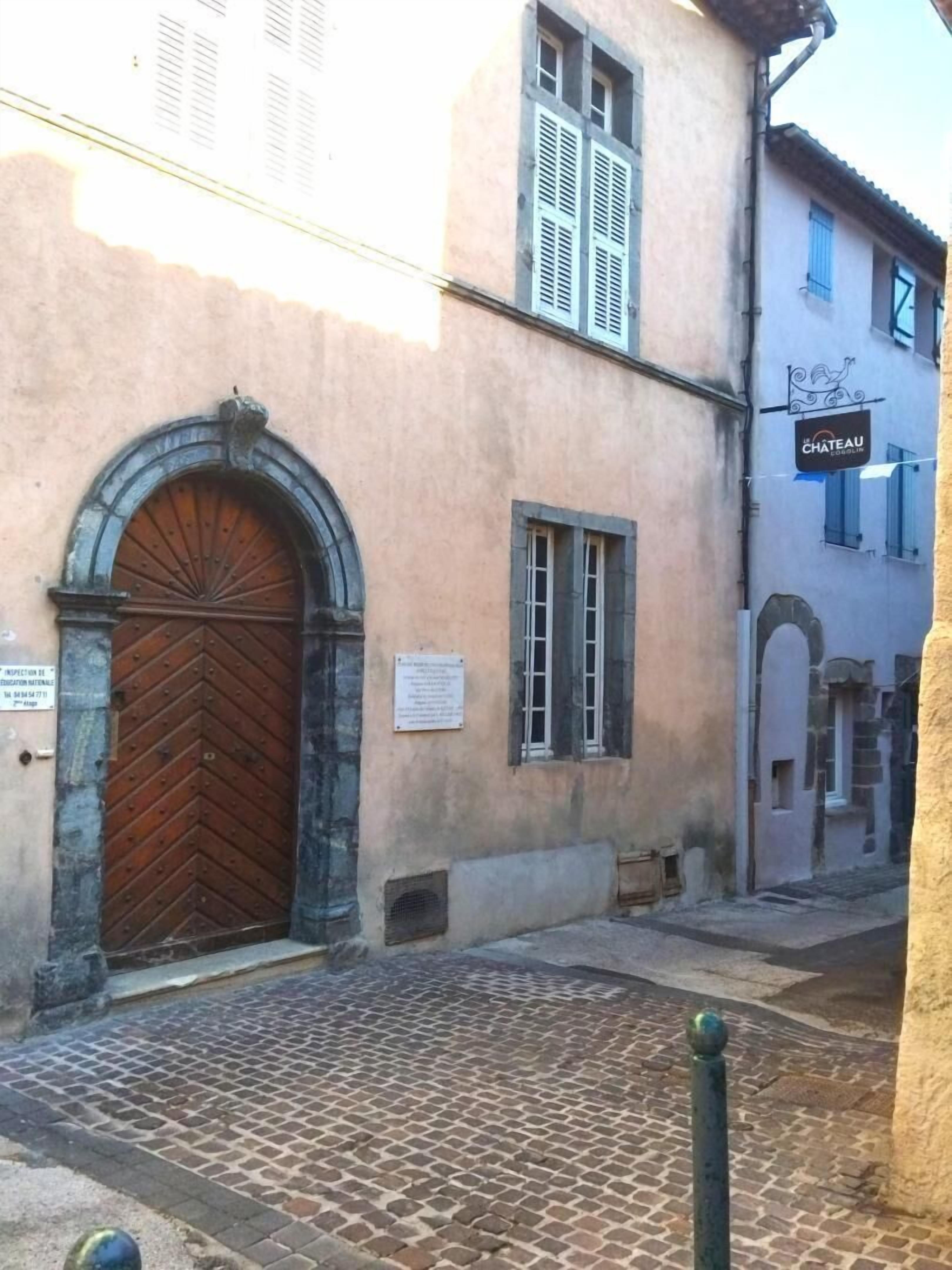 Un edificio con un'ampia porta in legno, un cartello con la scritta 'CHATEAU', e una strada acciottolata.