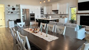Une cuisine moderne avec des meubles blancs, des appareils en acier inoxydable et un coin repas comprenant une table en bois foncé et des chaises blanches.