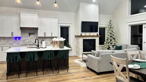 Une cuisine moderne avec des meubles blancs, un îlot central doté de tabourets de bar, une cheminée et un sapin de Noël.