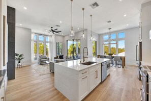 Una cocina amplia con una isla grande, modernos focos colgantes y vistas al exterior.