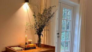 Eine Holzkommode mit Schubladen, eine Vase mit Trockenblumen und eine beleuchtete Wandleuchte.
