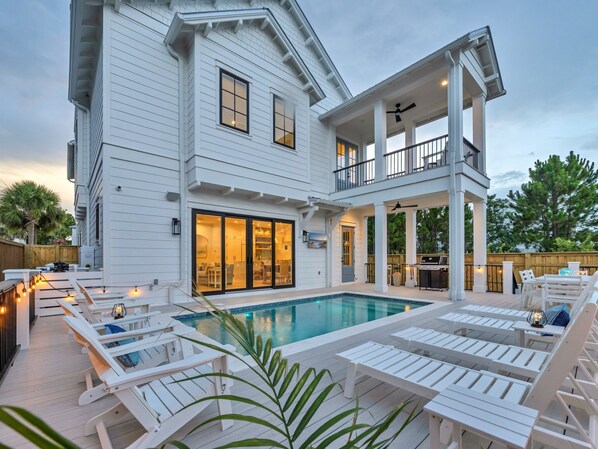 A two-story house with a pool, outdoor seating, and a covered patio area.