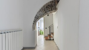 Un pasillo con un radiador blanco, un arco de piedra y una escalera que sube a otra habitación.