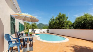 Piscina con sombrilla, mobiliario exterior y vistas a montañas.