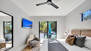 Ein modernes Schlafzimmer mit einem großen Bett, einem Deckenventilator, einem Fernseher und einer Schiebeglastür, die auf einen Balkon führt.