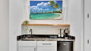 Eine Küche mit Kaffeebereich, einem Kühlschrank und einem an der Wand montierten Fernseher, der eine Strandansicht zeigt.