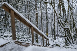 A wooden staircase in a snowy forest with a yellow sign on a tree. - Cozy Winter House • Hot Tub • Games • Sleeps 10 (Rhododendron)