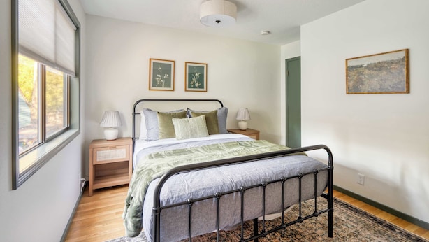 A bedroom with a metal bed frame, a wooden nightstand, a bedside table, a lamp, and two framed pictures on the wall.