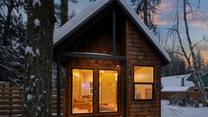 A wooden cabin with a warm interior, large windows, and a snow-covered landscape.