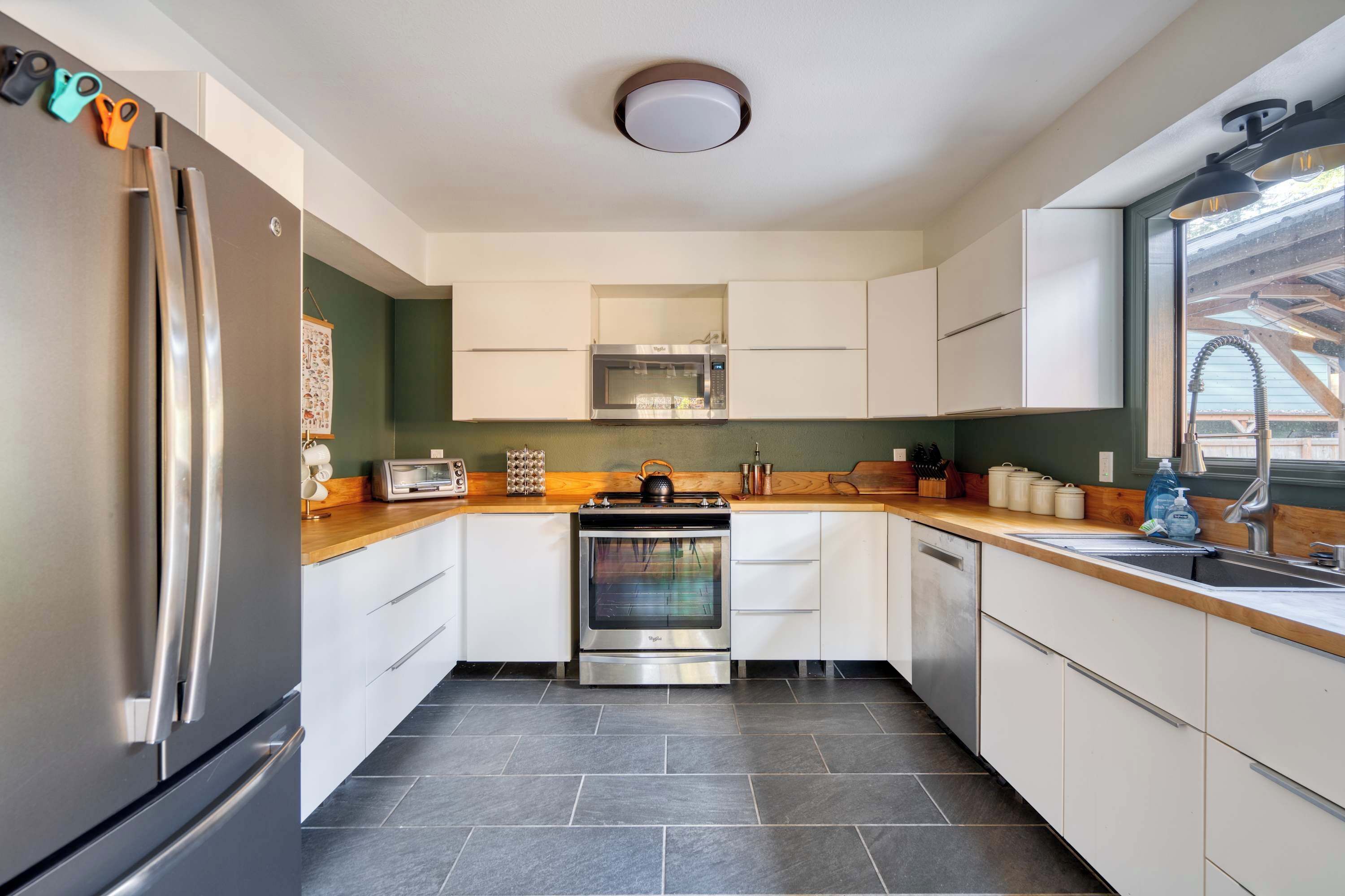 Eine moderne Küche mit einem Edelstahlkühlschrank, einem eingebauten Backofen und einer Mikrowelle. Es gibt eine Holz Arbeitsplatte, eine Spüle und Schränke.