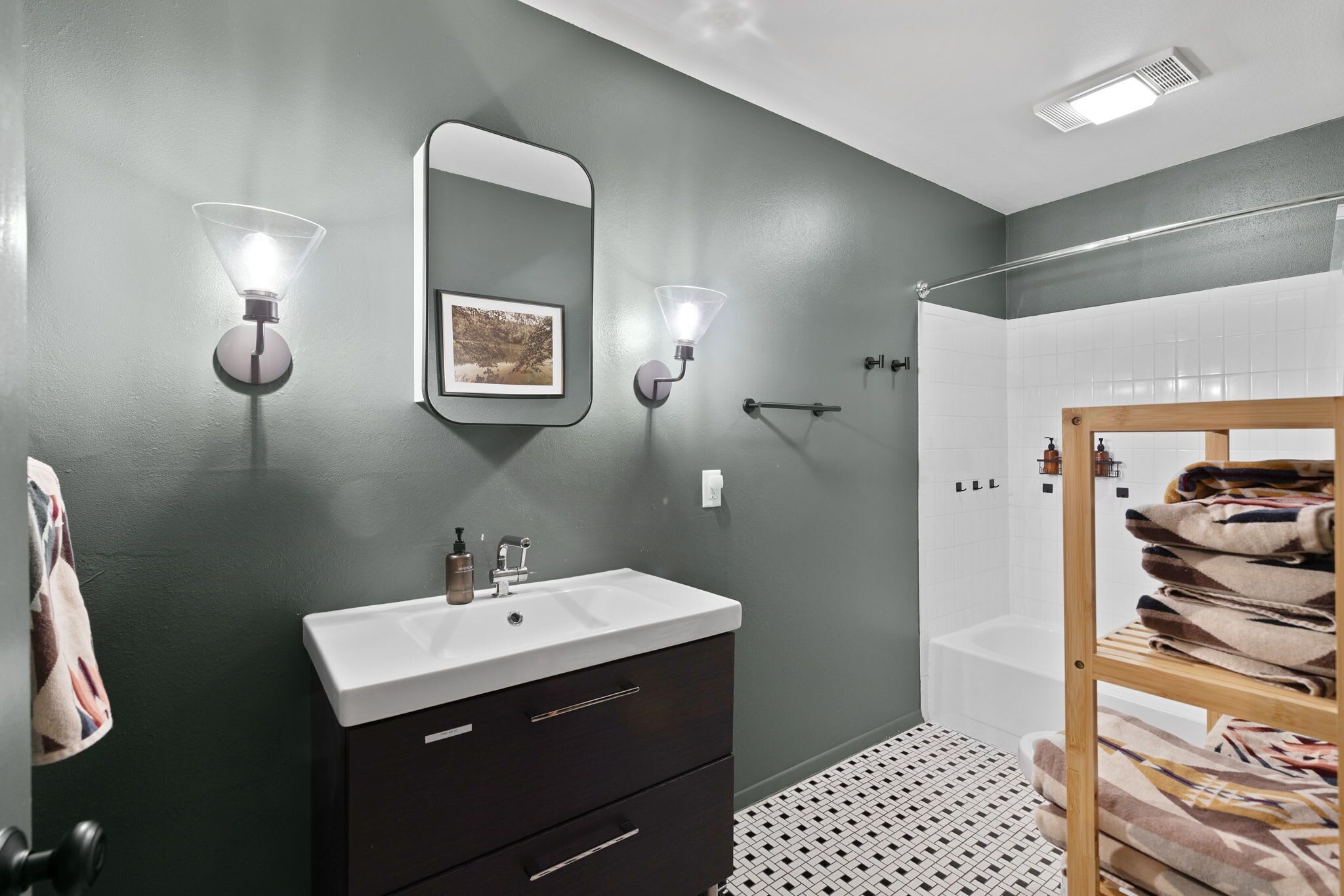 A modern bathroom with a dark green wall, a white sink, a mirror, and a towel rack with towels.