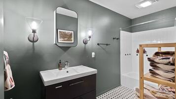 A modern bathroom with a dark green wall, a white sink, a mirror, and a towel rack with towels.