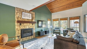A modern living room with a stone fireplace, comfortable seating, and large windows offering a view of the outdoors.