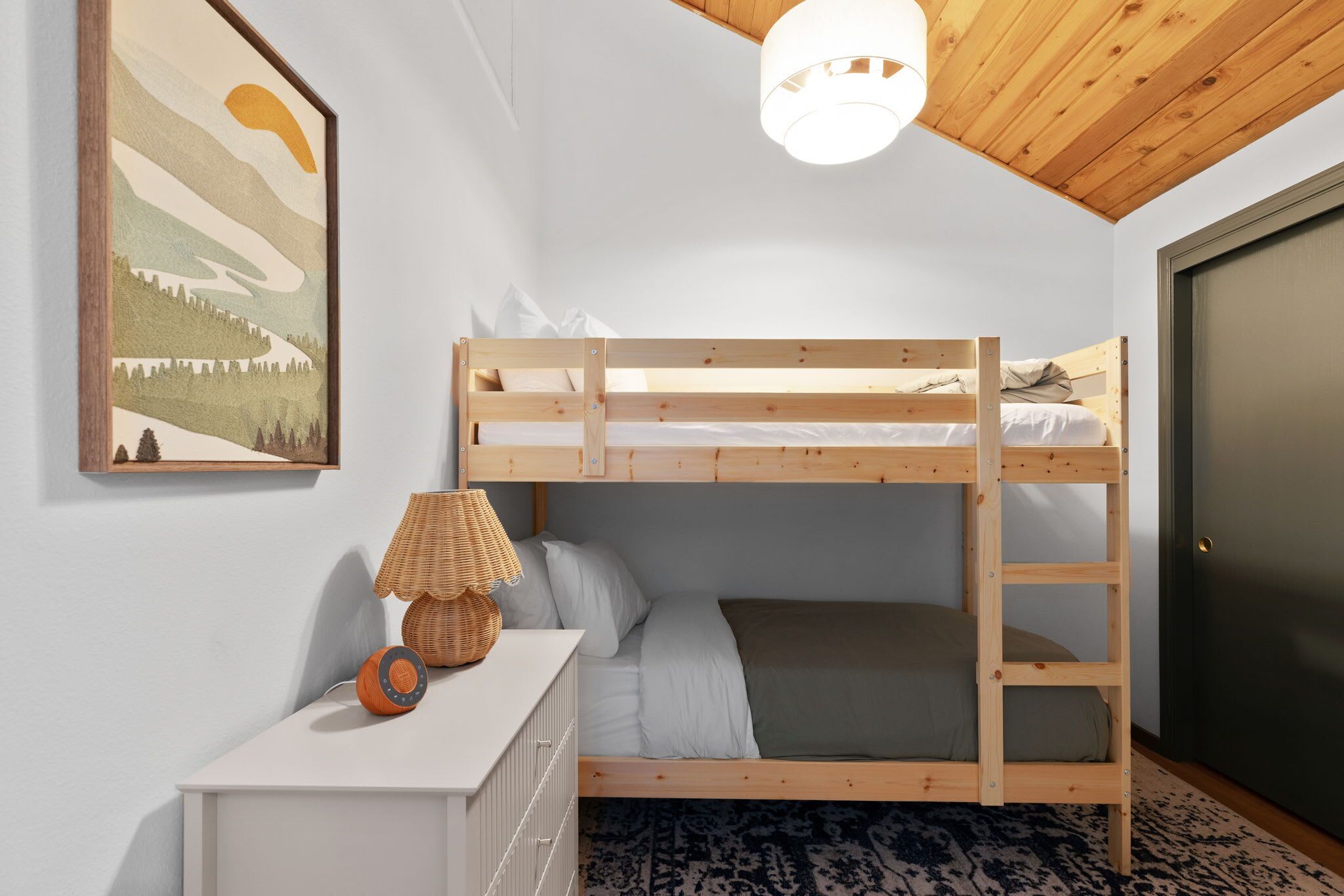 Camera con letto a castello, soffitto in legno, lampada a parete e quadro incorniciato.