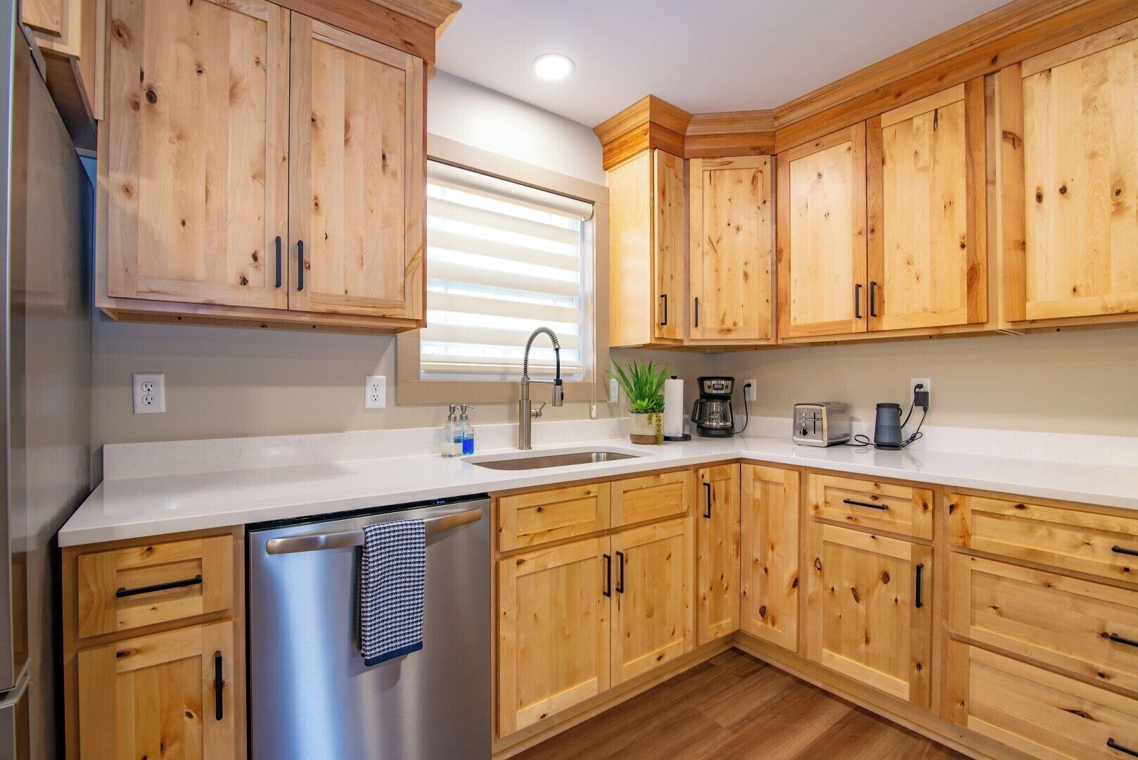 A kitchen with wooden cabinets, a stainless steel dishwasher, a sink, a coffee maker, and a toaster.