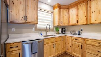 A kitchen with wooden cabinets, a stainless steel dishwasher, a sink, a coffee maker, and a toaster.