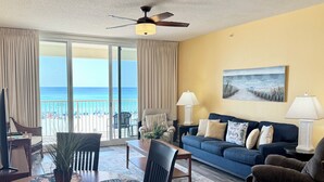 A living room with a view of the beach, a ceiling fan, and a blue sofa. - 🏖️Beach Chair Service Included-Beachfront @ Majestic Beach-Amazing View! (Panama City Beach)