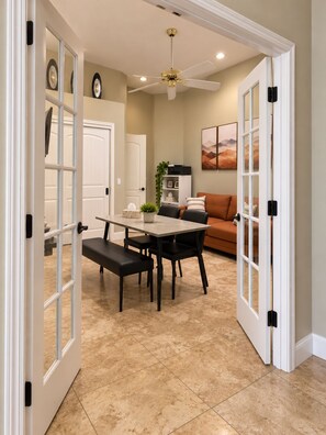 A dining area with a table and chairs, a ceiling fan, and a sofa in the background.