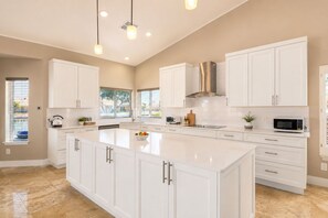 A modern kitchen with white cabinetry, a large island, stainless steel appliances, and pendant lighting. - 3-bedroom Lake front villa in Casa Grande. with heated pool & spa. Kayak & bikes (Casa Grande)
