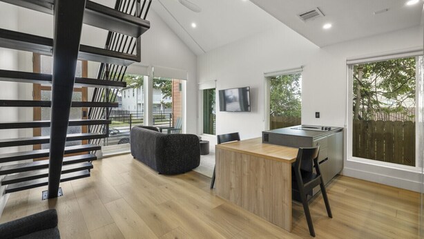 A modern kitchen with a central island, a dining area with a table and chairs, and a staircase with a railing. - O`Four Lofts North, Unit A (Houston)