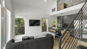 A modern living room with a black sofa, a flat-screen TV, and a staircase leading to an upper level. - O`Four Lofts North, Unit A (Houston)