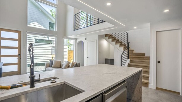 A modern kitchen with a large island, built-in dishwasher, and a staircase leading to an upper level. - The O'Four Lofts Cabin, Unit C (Houston)