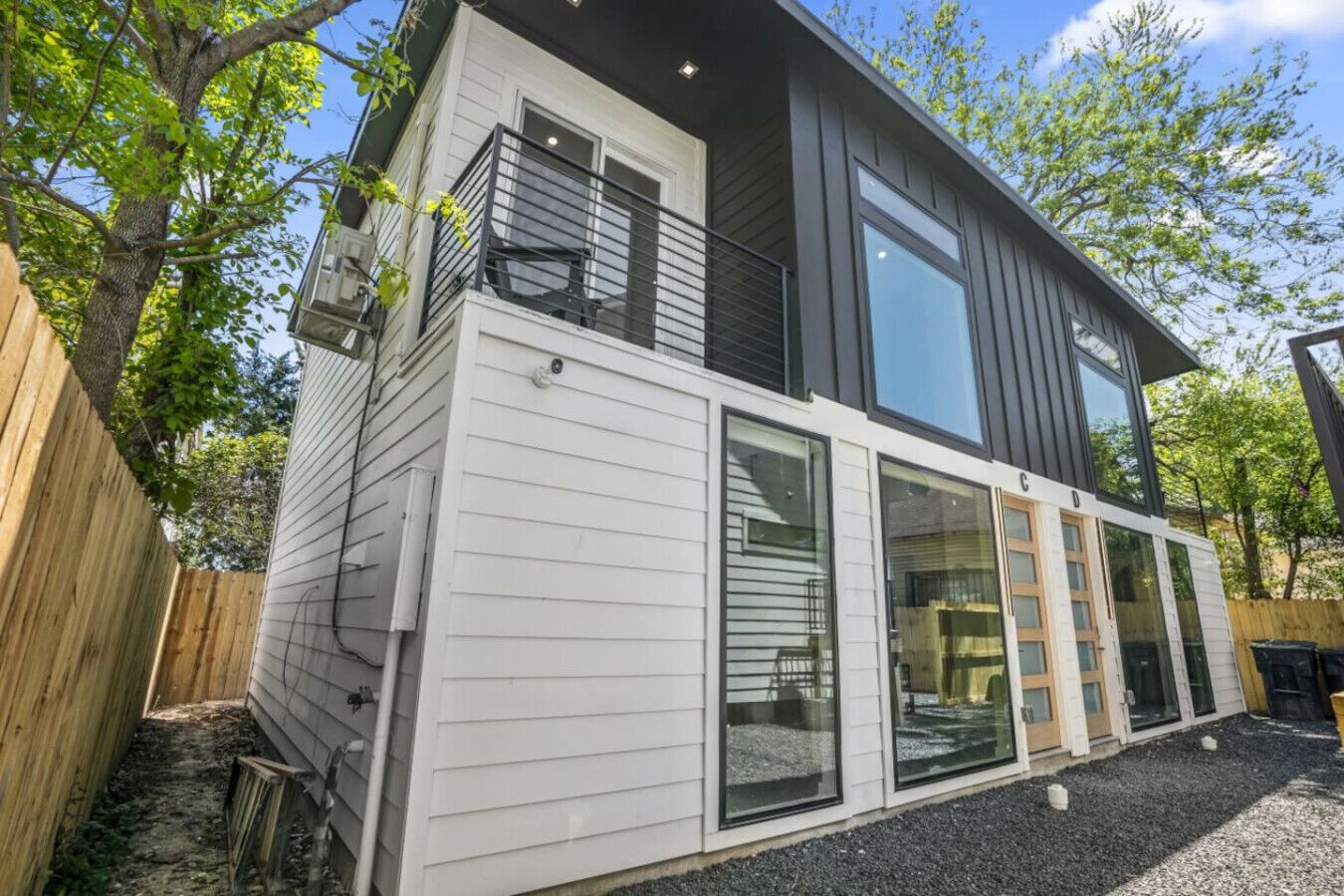 A modern two-story house with a balcony, large windows, and a wooden fence.