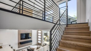 A modern interior with a staircase, a sofa, a TV, and a dining area. - The O'Four Lofts Cabin, Unit C (Houston)