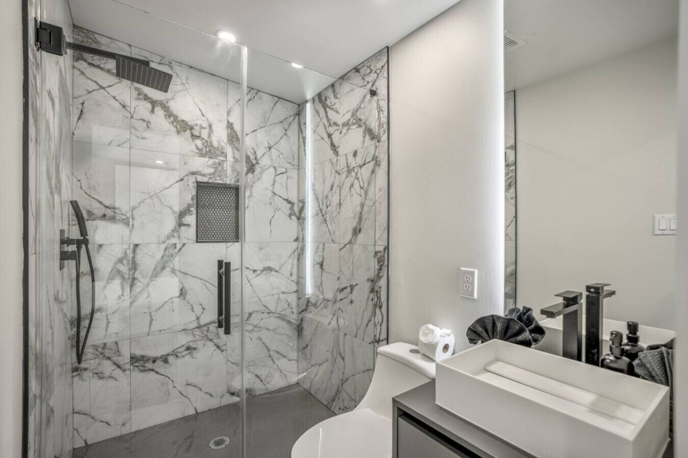 A modern bathroom with a glass-enclosed shower, marble walls, and a white vanity with a mirror.