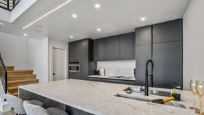A modern kitchen with a large island, dark cabinetry, and a stainless steel sink. - The O'Four Lofts Cabin, Unit C (Houston)