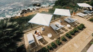 A rooftop terrace with lounge chairs, umbrellas, and a view of the ocean.