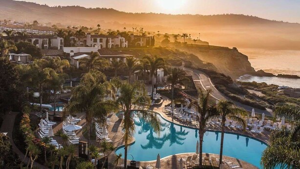 A resort with a pool, palm trees, and a view of the ocean at sunset.
