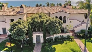 A Mediterranean-style villa with a terracotta-tiled roof, a central courtyard with a large tree, and a view of the sea.