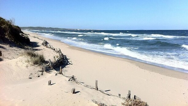 Ein Sandstrand mit einer Holzlattenzaun und Meereswellen.