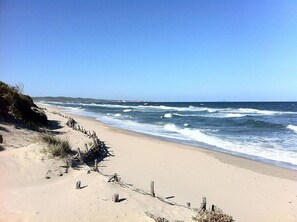 Une plage de sable avec une clôture en bois et des vagues de l’océan.