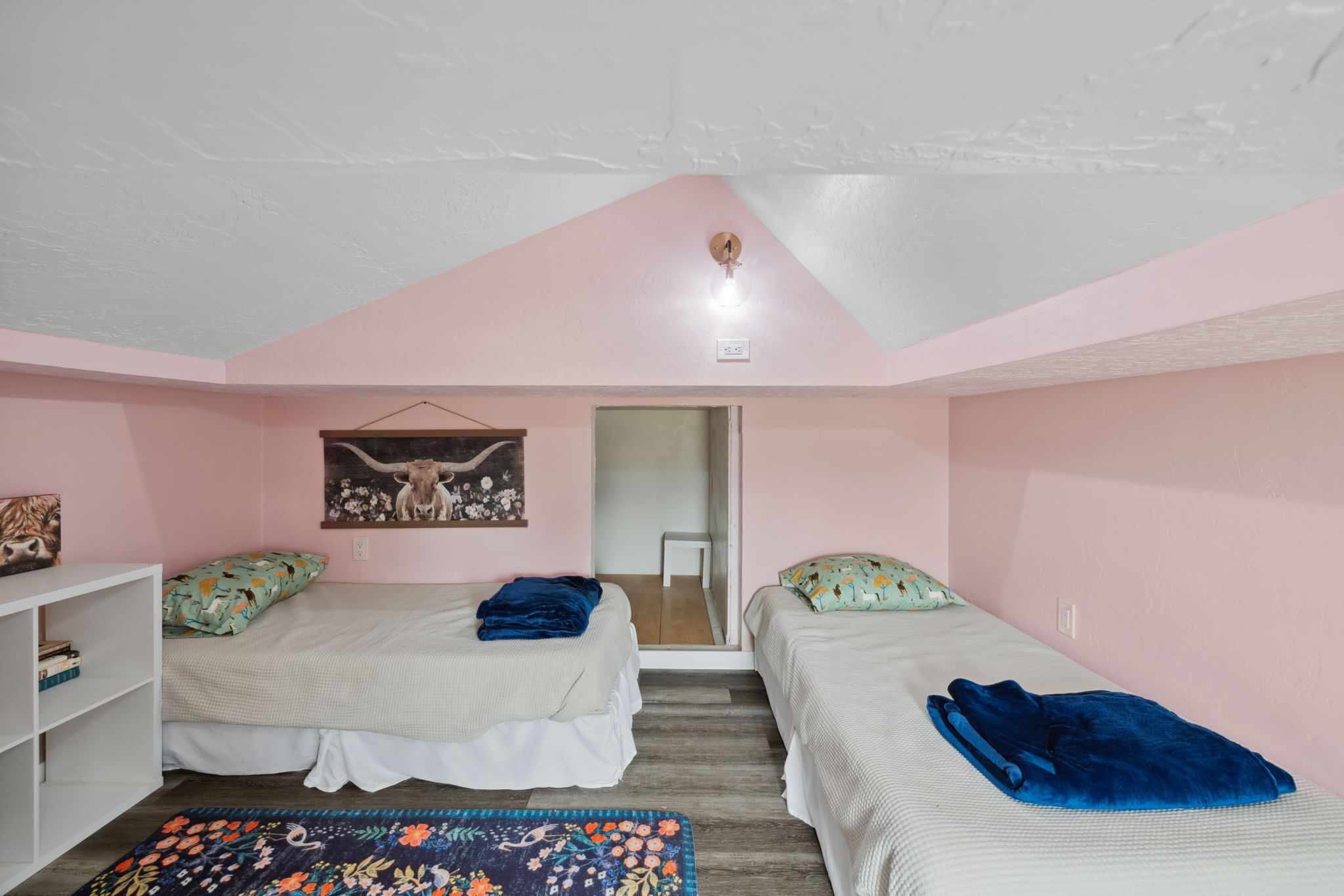 A bedroom with two beds, a white wardrobe, a hanging light fixture, and a door leading to another room.
