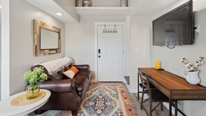 A modern living room with a brown leather sofa, a white door, a TV mounted on the wall, and a wooden dining table. - Charming barndominium with children's loft in quaint Middleton, Idaho (Caldwell)