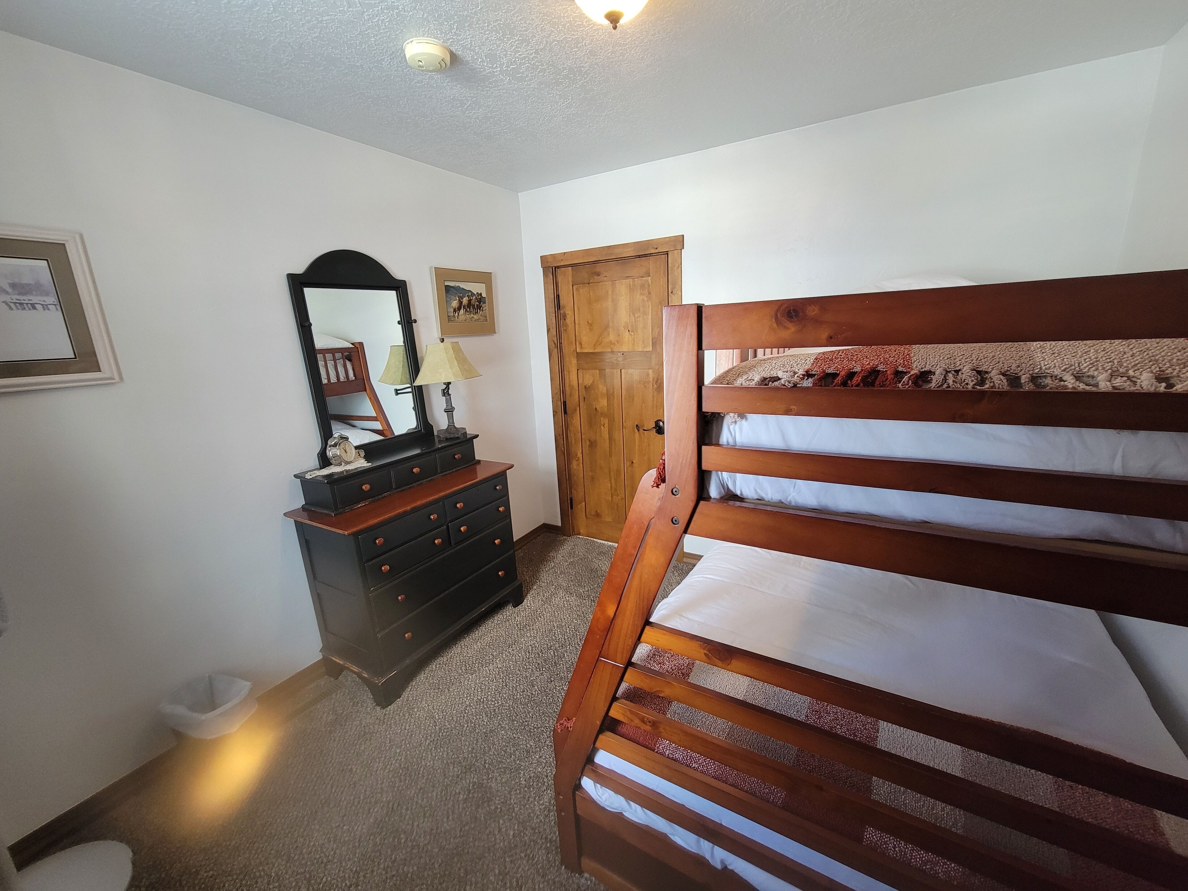 A bedroom with a wooden bunk bed, a dresser, a mirror, and a door.