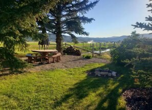 A picnic area with a table and benches, surrounded by grass and trees, with a view of distant hills. - Authentic pioneer
2 bedroom ranch farmhouse in beautiful Teton Valley Idaho. (Victor)
