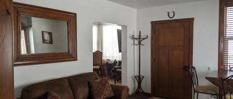 Uma sala de estar com um sofá de couro marrom, um aparador de madeira, uma mesa de jantar com cadeiras e um espelho grande na parede.