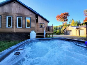 Ein Whirlpool vor einer Holzhütte mit einer Terrasse, umgeben von Bäumen mit Herbstlaub.