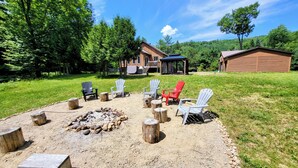 Un espacio de estar al aire libre rústico, con sillas Adirondack, un brasero y una mesa de piedra.