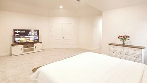 Une chambre spacieuse avec un grand lit, un téléviseur posé sur un meuble et une commode avec des tiroirs.