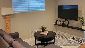 A modern living room with a sectional sofa, a round coffee table, a flat-screen TV, and a patterned rug.