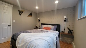 A bedroom with a bed, bedside lamps, a nightstand, a door, and a patterned wall.