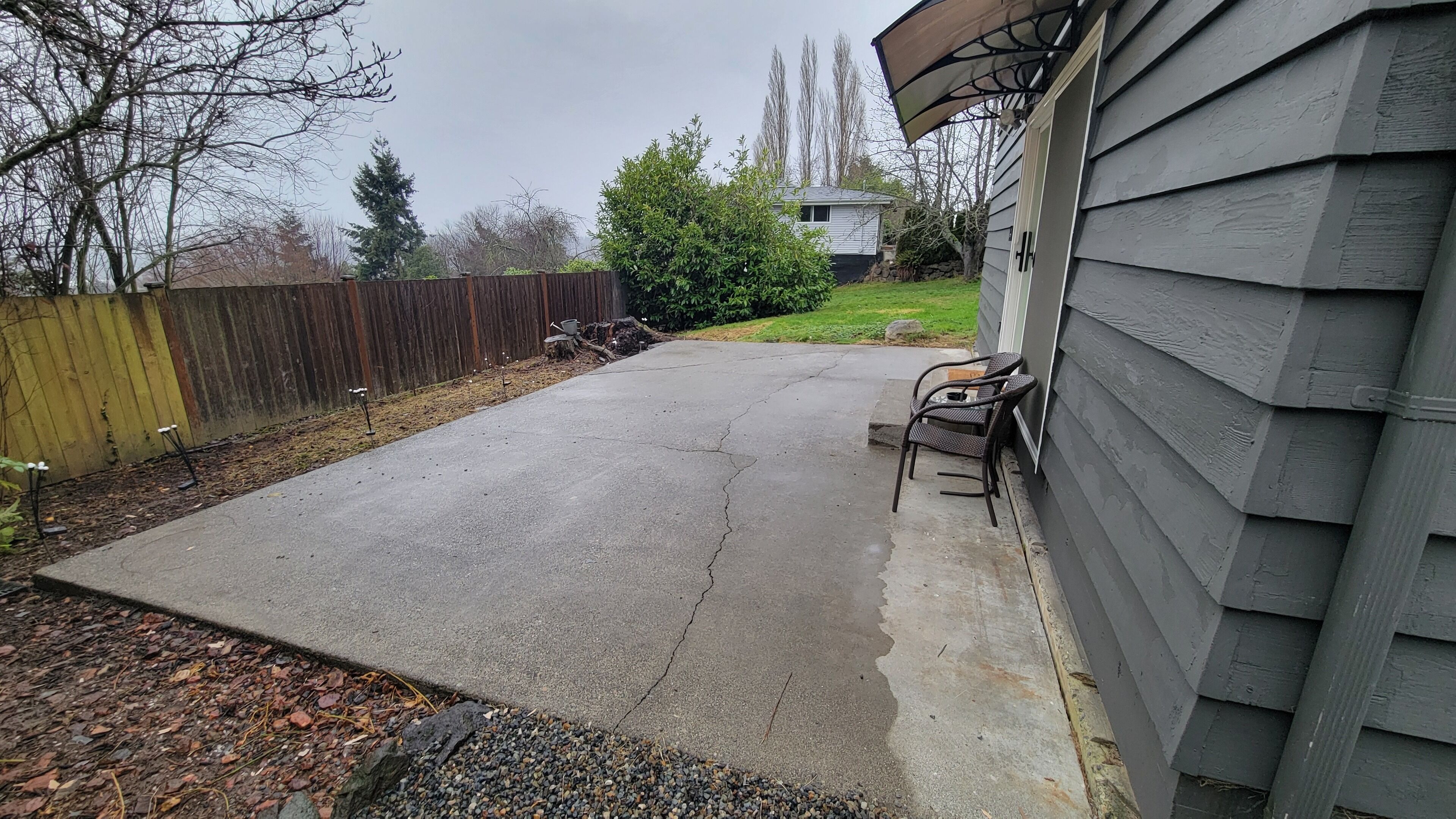 A residential backyard with a concrete patio, a wooden fence, and a house with siding.