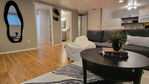 Ein Wohnzimmer mit einer Couch, einem Couchtisch mit Büchern, einem Zebra-Teppich und einem Küchenbereich im Hintergrund.